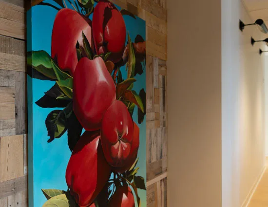 A tall painting of red apples on a blue sky, hung on a reclaimed wood wall