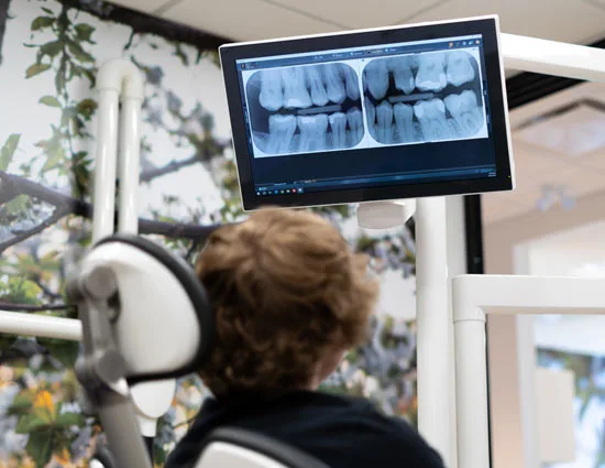 A patient in the chair looking at their x-rays on a screen, orchard wallpaper behind